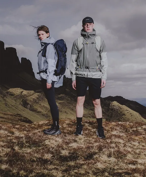 Zwei Wandernde mit Rucksack, Jacke und Salomon Wanderschuhen stehen auf einem Hochplateau vor Felsgipfeln